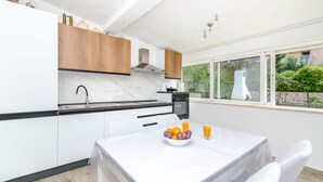 A modern kitchen with white cabinets, a marble countertop, and a dining area with a table set for two. - Apartment Close to the Beach (Stari Grad)