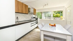 A modern kitchen with white cabinetry, a wooden upper section, and a dining area with a table and chairs. - Apartment Close to the Beach (Stari Grad)
