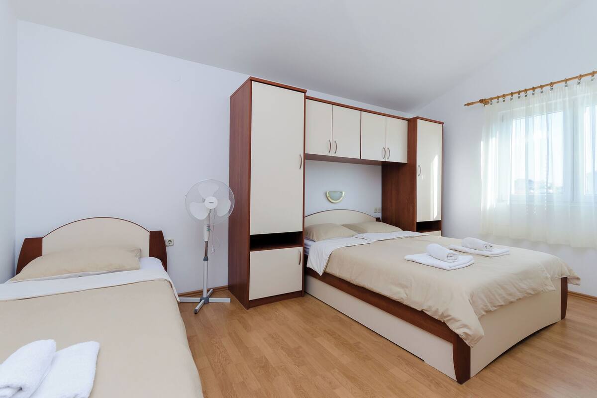 A hotel room with two beds, a wardrobe, a fan, and a window with curtains.