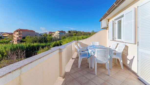 Ein Balkon mit Tisch und Stühlen mit Blick auf eine Wohngegend mit Häusern und viel Grün.