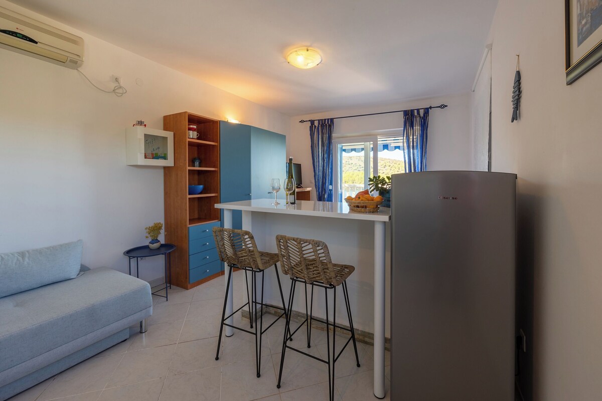 Ein gemütlicher Wohnraum mit Küchenzeile, einer Couch, zwei Barhocker und einem Kühlschrank.