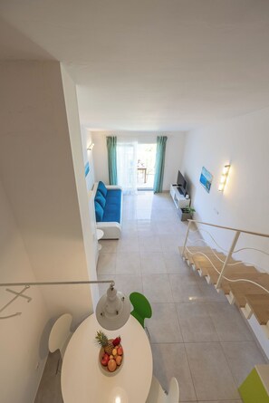 Ein modernes Wohnzimmer mit einem blauen Sofa, einem Esstisch mit Obst und einer Treppe, die in einen anderen Raum führt.