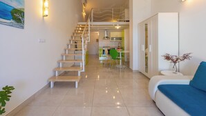 Un interior moderno con una escalera que lleva a una zona de altillo, un comedor y un espacio de estar con un sofá y una pequeña mesa.