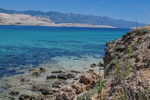 A coastal landscape with clear blue waters, rocky terrain, and distant mountains. - House Silvijo (Pag)