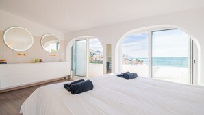 Een moderne hotelkamer met een groot bed, twee ronde spiegels, een kaptafel met spiegel, en een balkon met uitzicht op zee.