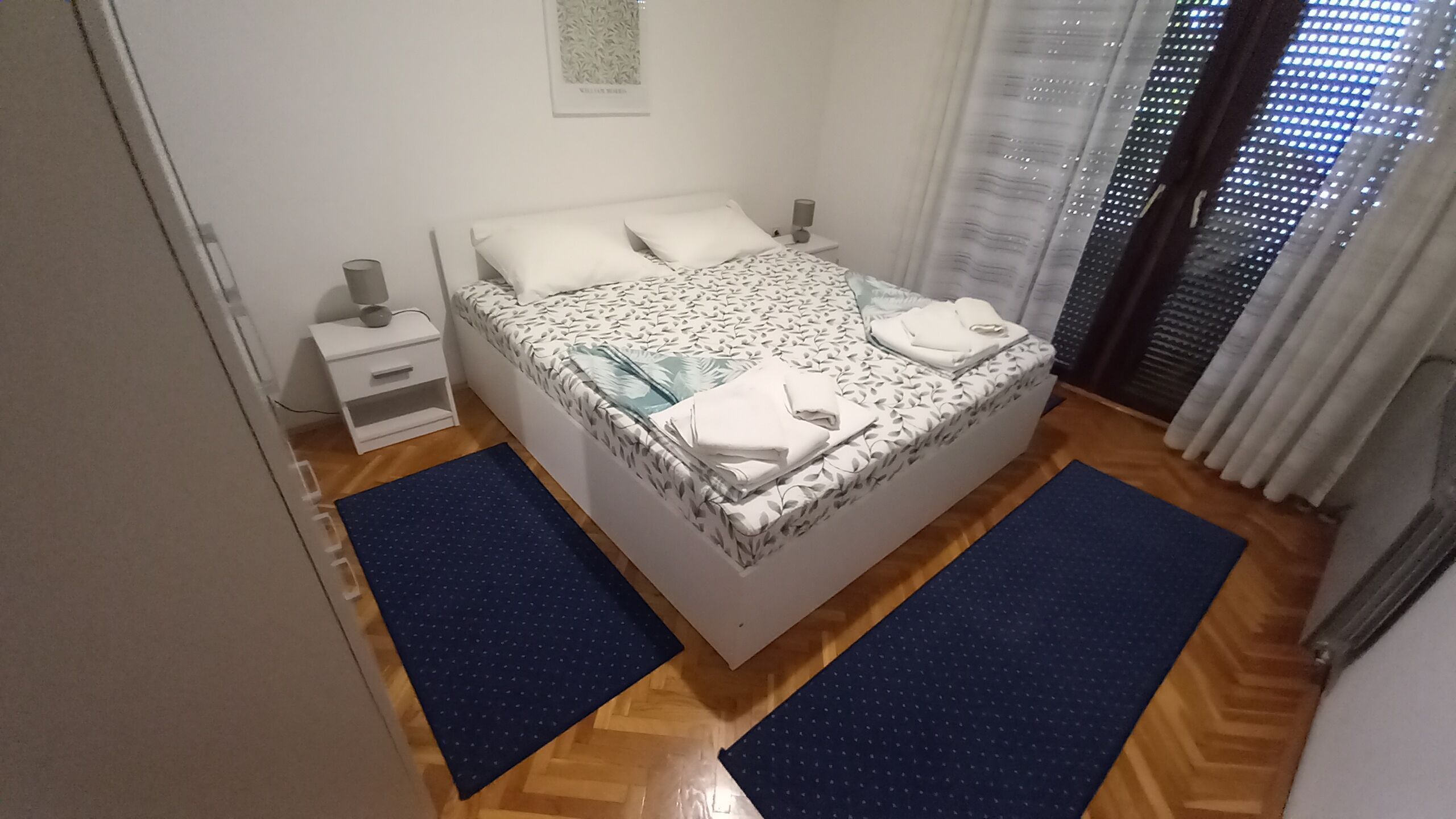 Un dormitorio con cama, mesita de noche, lámpara y ventana con cortinas.