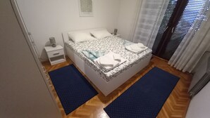 Ein Schlafzimmer mit Bett, Nachttisch, Lampe und einem Fenster mit Vorhängen.