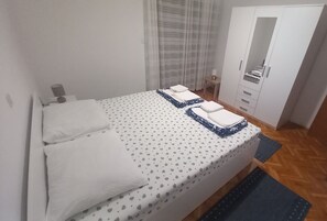 A neatly made bed with white and patterned bedding, a bedside table with a lamp, and a wardrobe with a mirror. - Apartments Vukelic (Crikvenica)