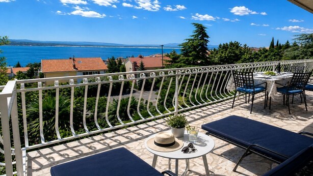 Ein Balkon mit Meerblick, einem Tisch mit Stühlen und einem kleinen Blumentopf.