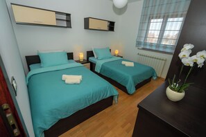 A hotel room with two beds, each with teal bedding and white towels, a wooden floor, a radiator, and a window with sheer curtains. - Apartment Istria (Vizinada)
