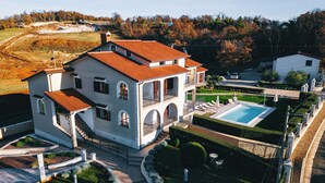 A large, two-story house with a swimming pool, surrounded by well-maintained gardens and a hilly landscape. - Apartment Istria (Vizinada)