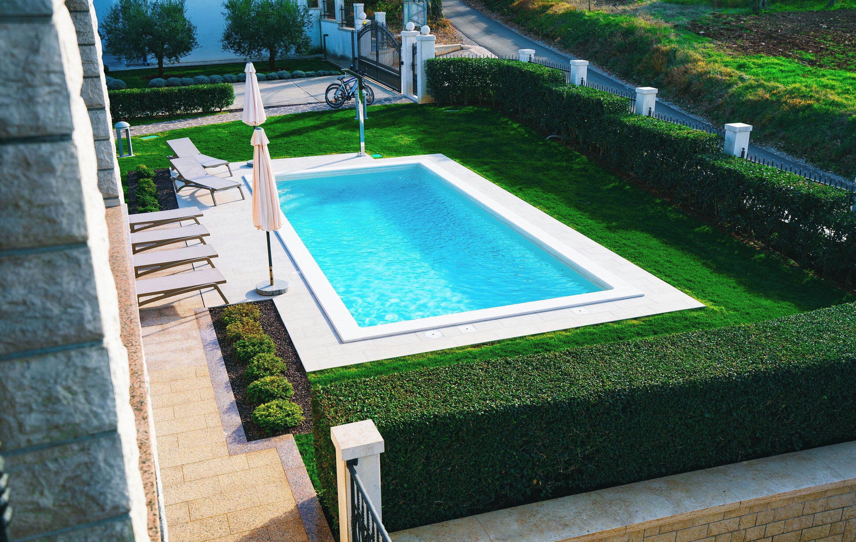 A rectangular swimming pool with a white border, surrounded by a well-manicured lawn and a stone wall.