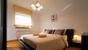 A bedroom with a large bed, a bedside table with a lamp, a window with blinds, and a wall-mounted artwork. - Apartment Istria (Vizinada)