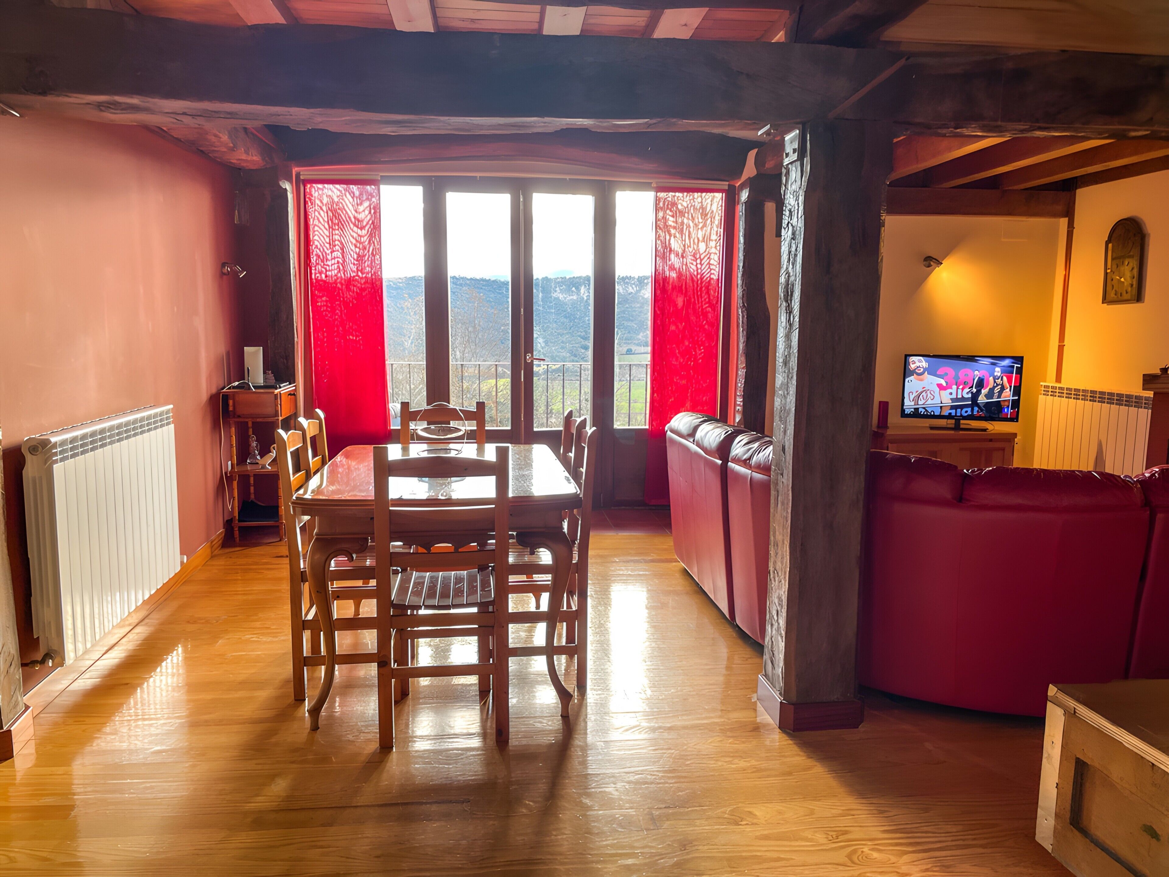 Un comedor con una mesa y sillas de madera, un sofá rojo y un televisor.