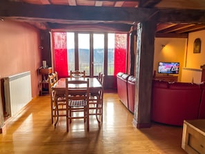 A dining area with a wooden table and chairs, a red sofa, and a television. - Berrobiaenea Country House: Nature and Sustainability (Narcué)