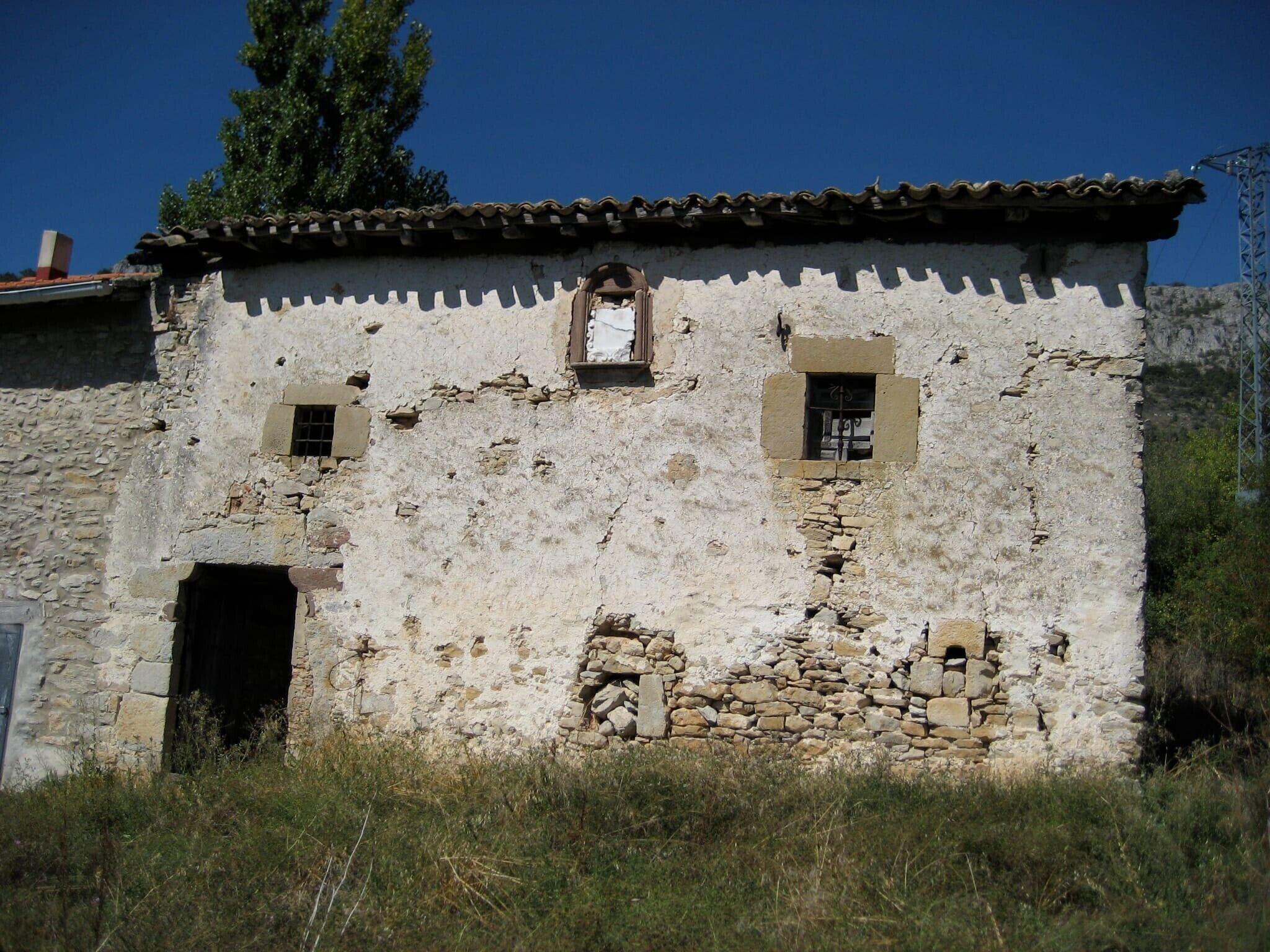 A rustic stone building with a tiled roof, two small windows, and a door.