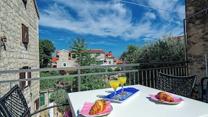 Ein Balkon mit Frühstückstisch, ausgestattet mit Croissants und Orangensaft, mit Blick auf eine malerische Stadt und historische Gebäude.