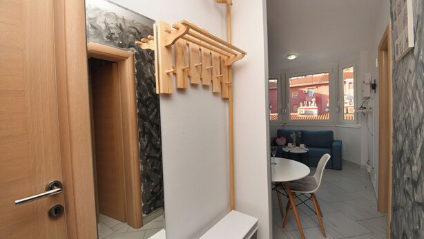A modern kitchen with a wooden rack, a white countertop, and a dining area with a table and chairs. - Apartment Corina (Rijeka)