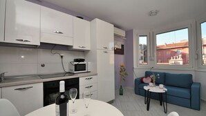 A modern kitchen with white cabinets, a microwave, and a wine bottle on the counter. - Apartment Corina (Rijeka)