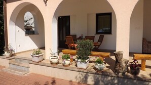 Un espace extérieur abrité, aménagé avec plusieurs bancs en bois et des plantes en pot.
