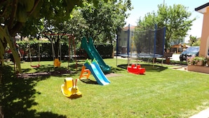 Une aire de jeux avec un toboggan, des balançoires et un trampoline.