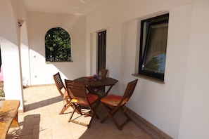 A patio with a round wooden table and four wooden chairs with orange cushions. - Apartments Valter (Umag)