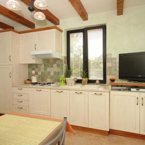 A kitchen with white cabinets, a gas stove, a sink, and a television. - Apartments Valter (Umag)