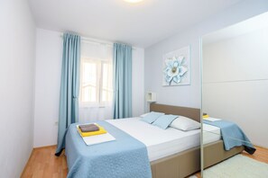 A bedroom with a bed, a bedside table, a mirror, and a window with curtains. - Apartment Sea View (Labin)
