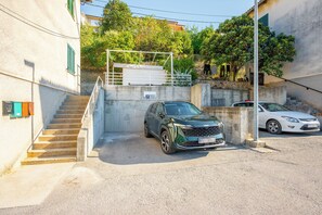 Un espace de stationnement où sont garées une voiture verte et une voiture blanche, un escalier menant à un bâtiment et un panneau indiquant un espace de stationnement réservé.