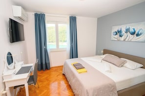 A hotel room with a bed, a desk with a computer, a TV, and a painting on the wall. - Apartment Sea View (Labin)