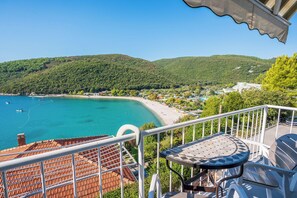 A balcony with a view of a turquoise sea, a beach, and green hills. - Apartment Sea View (Labin)