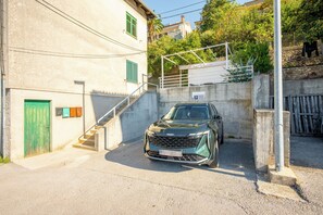 Une voiture est garée dans une allée, et un escalier mène à l’entrée d’un immeuble.