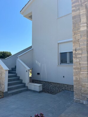 Ein modernes, zweistöckiges Haus mit einer Steinwand und einer Treppe aus Beton. Ein kleines Fenster ist ebenfalls zu sehen.