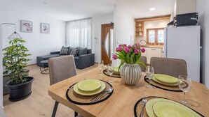 Una sala moderna con sofá, una mesa de comedor para dos personas y una cocina al fondo.