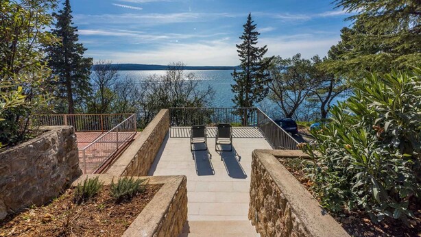 Una terraza con vistas a un lago, muros de piedra y mobiliario exterior.