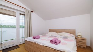 A bedroom with a wooden bed, a nightstand, and a view of a lake through a glass door. - Apartments Anica J (Lopar)