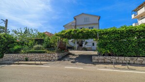 A residential street with a house featuring a stone wall, a metal gate, and a clear blue sky. - Apartments Anica J (Lopar)