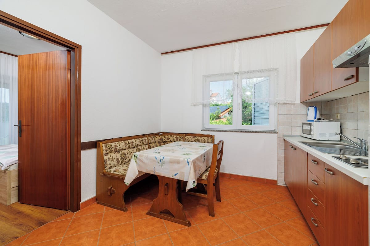 A compact kitchen with a dining table, wooden cabinets, and a window with curtains.