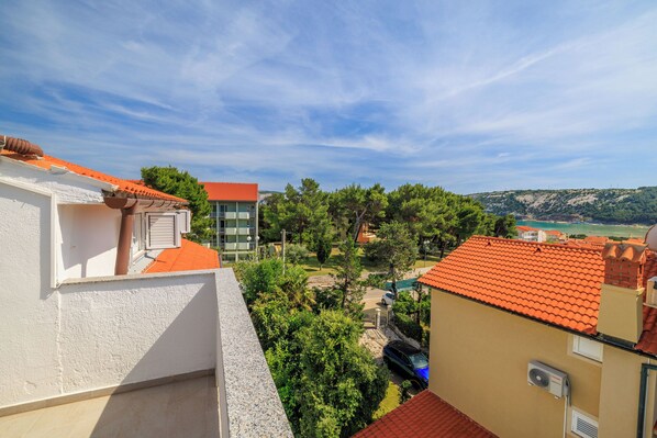 A residential area with a view of a building with a red-tiled roof, surrounded by greenery and a clear sky. - Apartments Anica J (Lopar)