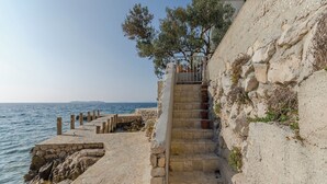 Una escalera de piedra conduce a una terraza frente al mar, con vista despejada del océano y una masa de tierra a lo lejos.