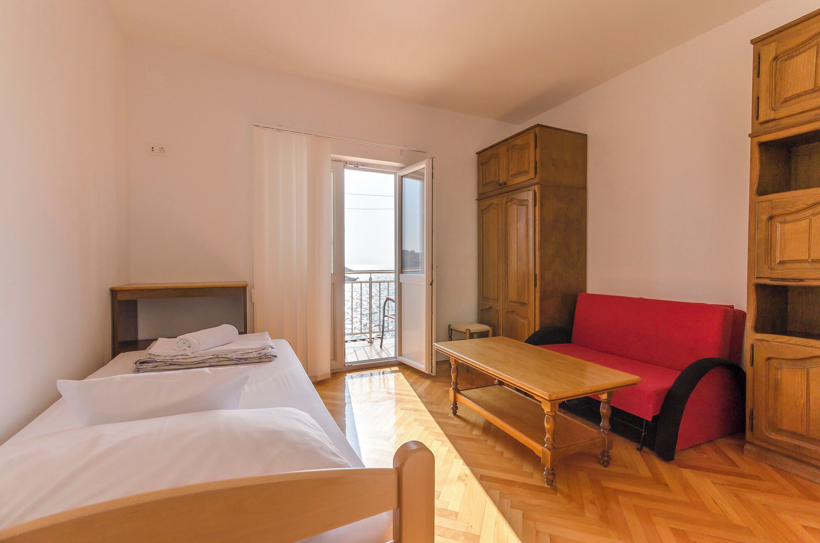 Une pièce comprenant un lit, un canapé rouge, une table en bois et une armoire.