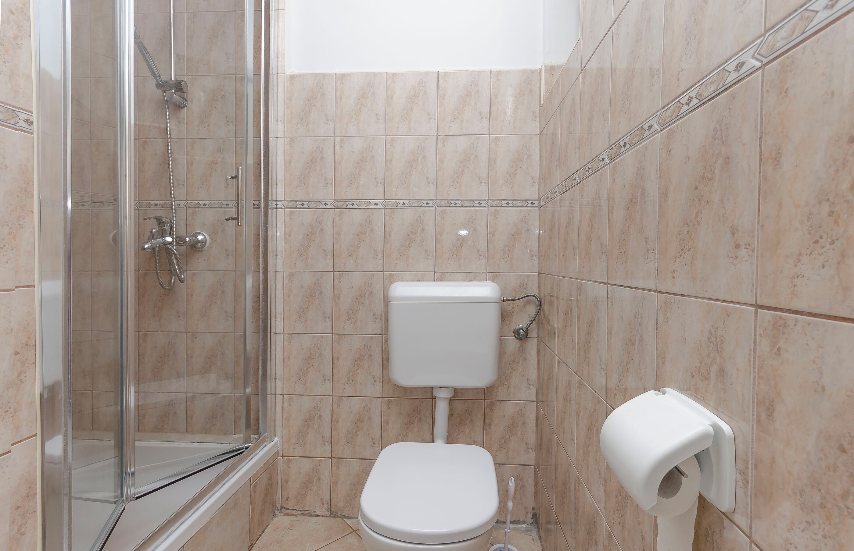 A bathroom with a glass shower enclosure, a toilet, and a paper towel dispenser.