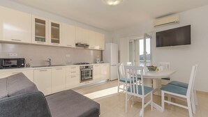 Una cocina moderna con armarios blancos, un microondas, estufa y refrigerador. Hay una mesa de comedor con sillas y un televisor de pantalla plana montado en la pared.