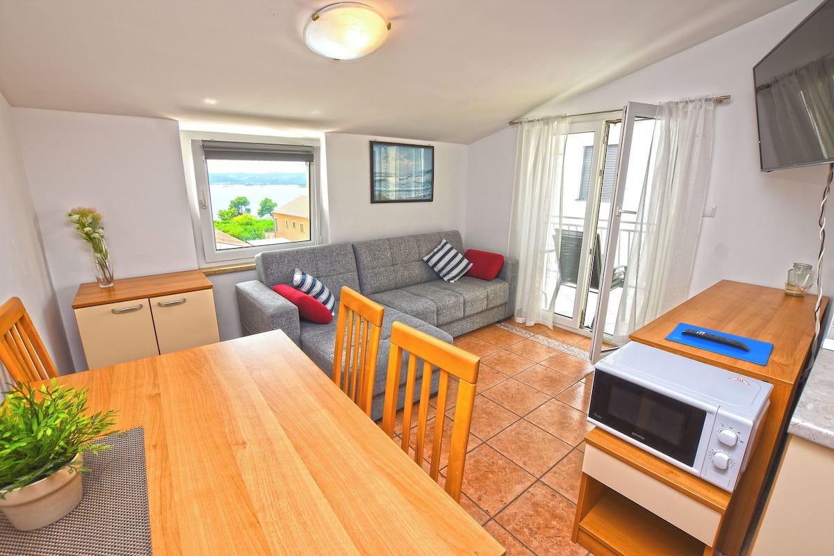 A compact living space with a dining area, a sofa, a kitchenette, and a view of the outdoors.