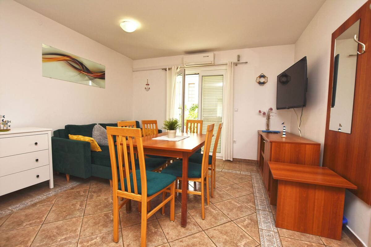A dining area with a wooden table and chairs, a sofa, a TV, and a small cabinet.