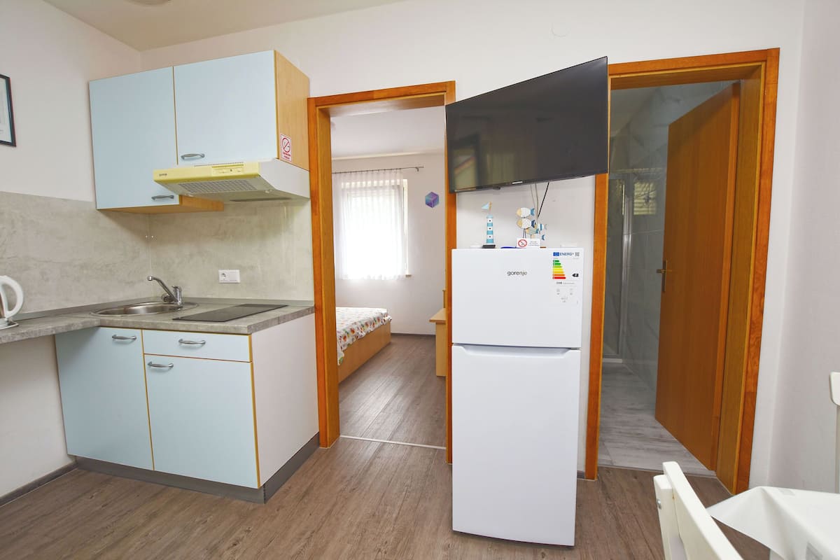 A compact kitchen with light blue cabinets, a white refrigerator, and a wooden door leading to a bedroom.