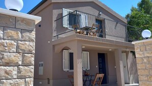 A two-story house with a stone facade, a balcony with a metal railing, and a small outdoor seating area with chairs and a table. - Apartments Hvaranin (Stari Grad)
