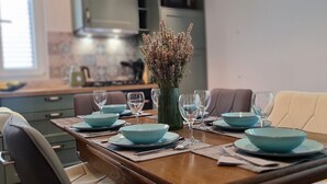 A dining table set with blue bowls and wine glasses, a vase with dried flowers, and a modern kitchen in the background. - Apartments Hvaranin (Stari Grad)