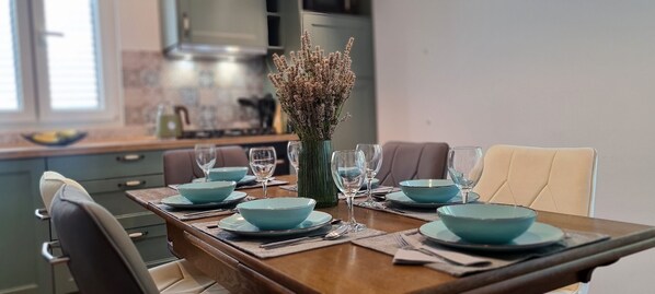 A dining table set with blue bowls and wine glasses, a vase with dried flowers, and a modern kitchen in the background. - Apartments Hvaranin (Stari Grad)