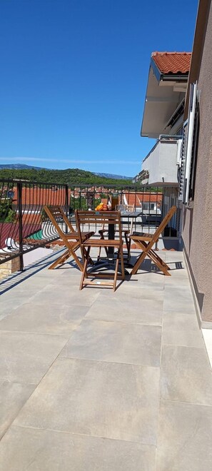 A balcony with a table and chairs, a tiled floor, and a view of buildings and hills in the background. - Apartments Hvaranin (Stari Grad)